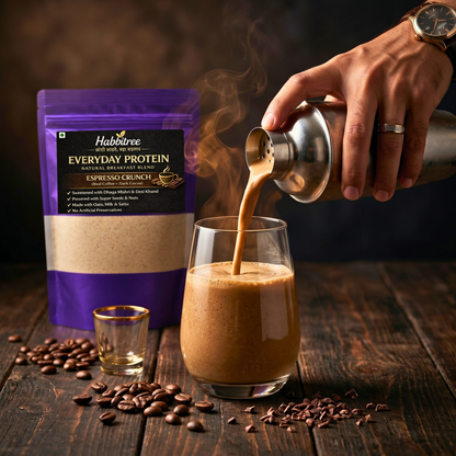 Creamy Habbitree Espresso Crunch everyday protein shake being poured into a glass with coffee beans, cocoa nibs and natural breakfast blend on wooden table